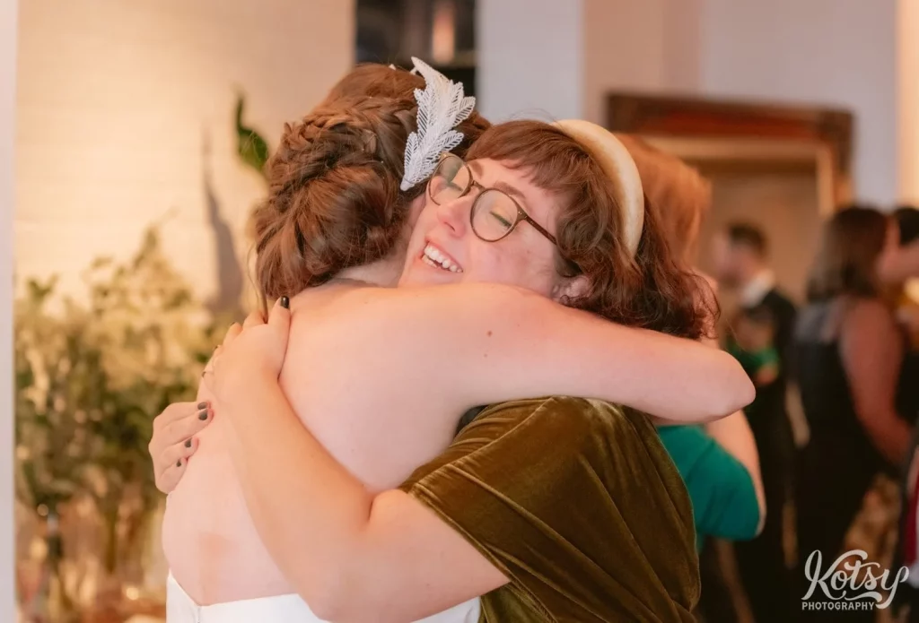 A woman with glasses hugs a bride and a white tiara and white wedding gown at the end of her Burroughes Building wedding ceremony in Toronto, Canada